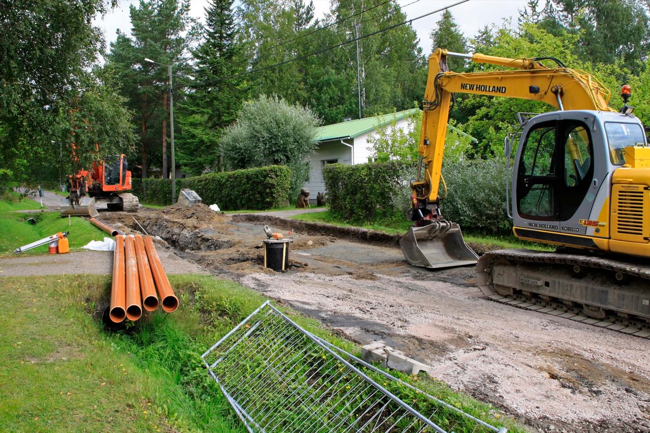 Kaivuri kaivaa omakotitalon vesiputkea maahan.