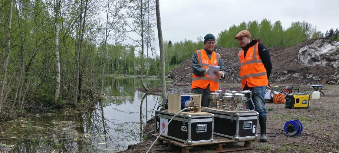 Mittalaite veden äärellä, kaksi ihmistä huomioliiveissä