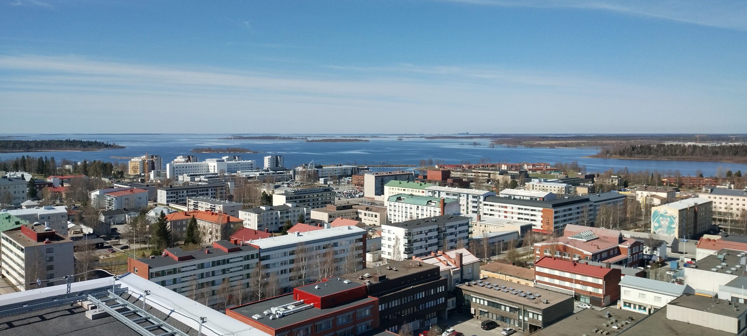 Kuvassa näkyy etualalla kerrostaloja ja kaupungin katuja, talojen takan näkyy sininen meri, saaria ja taustalla sininen taivas.